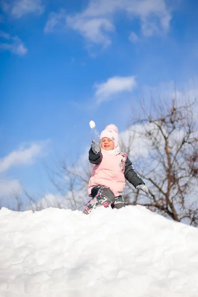 Маленька дівчинка грає у сніжки. Дитина розважається в сонячний зимовий день, грає і їде на сніговій гірці без санки і стрибає в снігоходи, зимовий пейзаж з блакитним небом — стокове фото