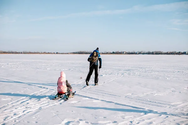 Familie auf Winterwanderung. Junger Mann und Kind fahren im Winter auf zugefrorenem Fluss in Waldnähe Ski, Mann rodelt Kind im Schnee — Stockfoto