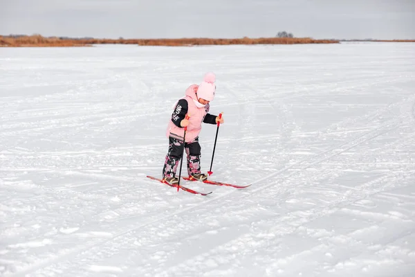 A menina está a esquiar. Criança de terno quente rosa aprende a esquiar neve no dia de inverno gelado, paisagem de inverno, fundo de neve — Fotografia de Stock
