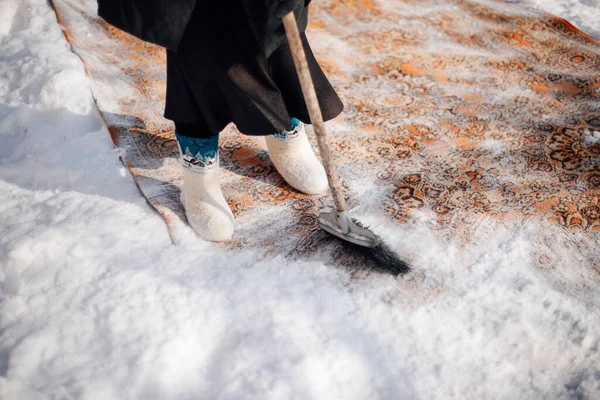 Tapis persan en gros plan. Méthode traditionnelle de nettoyage écologique des tapis poussiéreux avec de la neige fraîche et du balai, l'homme en bottes de feutre se tient dans la neige — Photo