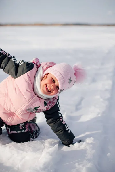 Дитина любить ходити на свіжому повітрі. Маленька дівчинка в рожевій зимовій куртці і капелюсі з помпоном розважається на природі і насолоджується сонячною погодою і грає зі снігом, крупним планом — стокове фото