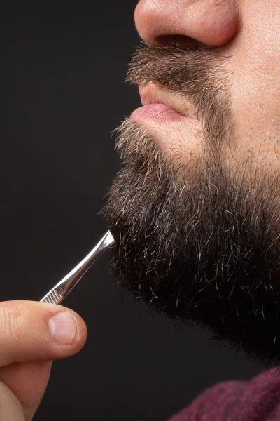 Perfil del hombre barbudo sacando dolorosamente el pelo gris de la barba gris con pinzas, emociones desagradables en la barbería — Foto de Stock