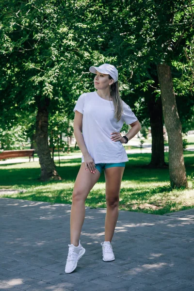 Retrato de una joven deportista posando en el parque en ropa deportiva con relojes a la mano en el soleado día de verano sobre el fondo de árboles verdes — Foto de Stock