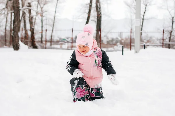 Kid looking at snow standing up from ground and smiling wearing pink winter clothes in park. Astonishing background full of white color and snow — Stockfoto