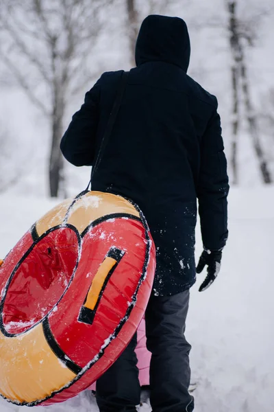 Photo rapprochée d'une jeune femme russe invisible derrière son père avec un traîneau montant la colline pour glisser dans la neige dans la forêt. Fond étonnant plein de couleur blanche et de neige — Photo