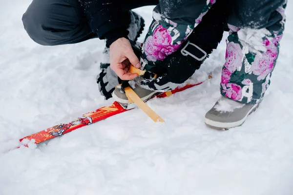 Photo en gros plan d'une fillette aidée par son père aimant à enfiler des skis sur des pieds d'enfant sans visage dans le cadre. Fond étonnant plein de couleur blanche et de neige — Photo