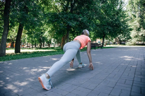 Pretty young sporty woman in park in sportswear warming up exercising stretching getting ready for starting — Stock Photo, Image