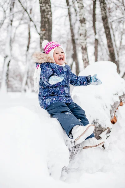Ağaç kütüğünde oturan mutlu bir kız çocuğu. Karla kaplı. Ellerini kaldırmış, gülümsüyor. Beyaz renklerle dolu muhteşem bir arkaplan