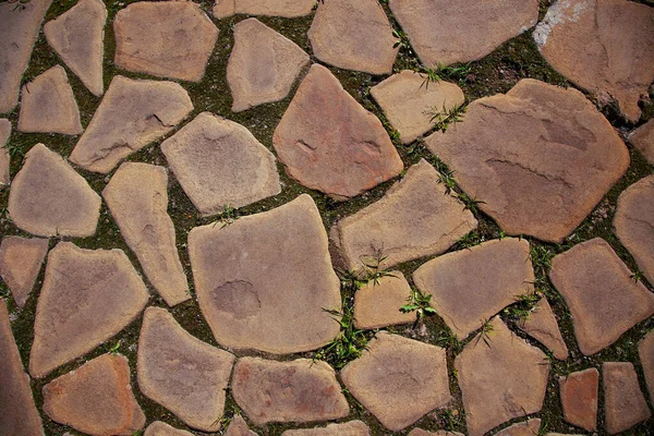 Ostrukturerad kaklad väg bestående av plana stenar som läggs i marken med naturlig textur med litet gräs mellan stenblock. Perfekt inte distraherande bakgrund — Stockfoto