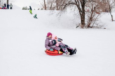 Kadın Rus çocuğun gülümsediği ve tepeden kayarak kaydığı ve büyükannesinin parkta sıcak kışlık kıyafetler giydiği bir fotoğraf. Beyaz renk ve karla dolu şaşırtıcı bir arka plan. 