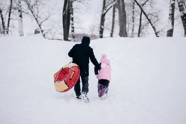 Foto distante di bambino e padre donna con slitta che sale in collina per scivolare giù nella neve nella foresta. Sfondo sorprendente pieno di colore bianco e neve — Foto Stock