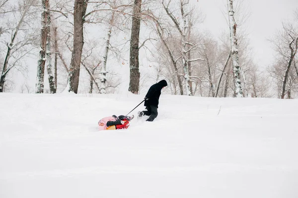 Kind liegt auf Schlitten, Vater zieht Tochter in pinkfarbener Winterkleidung im Wald. Erstaunlicher Hintergrund voller weißer Farbe und Schnee — Stockfoto
