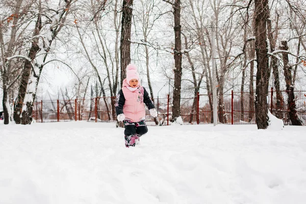 Kid walking in snow and smiling wearing pink winter clothes in park. Astonishing background full of white color and snow — Stockfoto