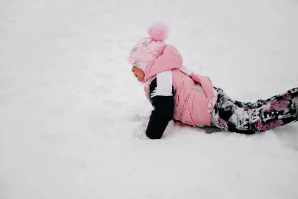 Крупним планом фотографія жінки, яка лежить і повзає в снігу, дивлячись в рожевий зимовий одяг в лісі. Дивовижний фон, повний білого кольору і снігу — стокове фото