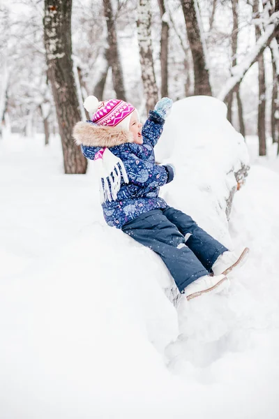 Захоплена маленька дівчинка на дереві, вкрита снігом, посміхається зубами, розмахуючи руками, і дивиться в теплий зимовий одяг в парку. Дивовижний фон, повний білого кольору — стокове фото