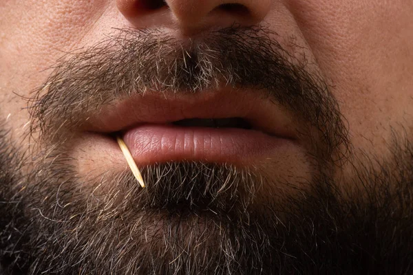Крупный план разгневанных губ, бородатое лицо человека с зубочисткой в зубах, злобные эмоции бандита, опасность и агрессия — стоковое фото