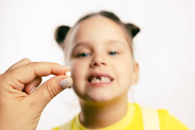 El ele tutuşmak, beyaz arka planda sarı tişörtlü bulanık küçük bir kızın olduğu geçici süt dişini sökmek. İlk dişler değişiyor. Diş tedavisi için dişçiye gidiyorum. 