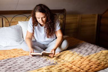 Kıvırcık, yetişkin bir kadın yatakta bağdaş kurarak oturuyor. Elinde kitap olan Terry yatak örtüsüyle. Hafta sonları ev kıyafetleri giyerek kitap okuyor. Evde dinlenme zamanı. 