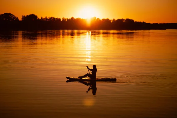 夏天，船桨手握在湖面上，背景是迷人的落日，覆盖着橙色的水。积极的生活方式 — 图库照片
