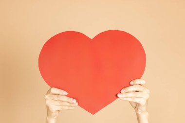 Deri renginin arka planında kalp şeklinde kırmızı kartpostal tutan kadın eller. Sevgililer Günü 'yle sevgilisini kutluyor ve tebrik ediyor. Aşkı ifade etmek