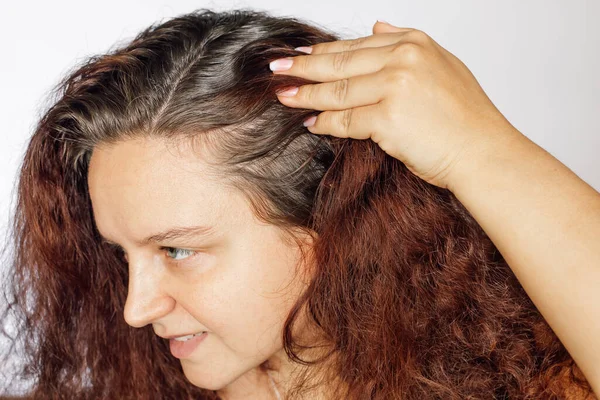 Женщина показывает седые корни волос, отталкивая левую сторону волос назад на белом фоне. Возродить корни, которые нуждаются в перекраске. Антивозрастной уход. Копирование пространства — стоковое фото