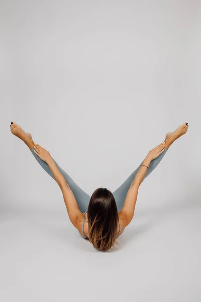 A mulher pratica desporto. Morena está fazendo exercício de ioga ou fitness, ela está deitada de costas com as pernas e braços levantados de cabeça para baixo, fundo isolado, visão traseira — Fotografia de Stock