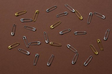 Fotoğrafın her tarafına koyu kahverengi arka plana yerleştirilmiş gümüş ve altın güvenlik iğneleri. Uzayı kopyala Fotoğrafçılığı taklit et. Ofis kırtasiyesiyle yaratıcı minimalizm 