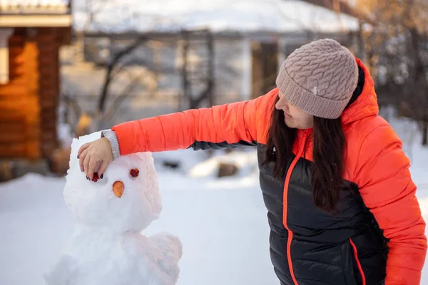 Medelålders kvinna att göra ansiktet av snögubbe med improviserade medel på dagtid samtidigt som man går på bakgård med träd, hus och starkt solljus i bakgrunden. Föräldrar som umgås med barn — Stockfoto