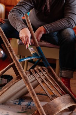 Ev atölyesinde mobilyaları yenilemek için fırçayla eski sandalyenin bacaklarını koyu maviyle boyayan bir bayan. Eski şeylerin tekrar kullanılması. Sürdürülebilir eylemlerle geleceği düşünmek