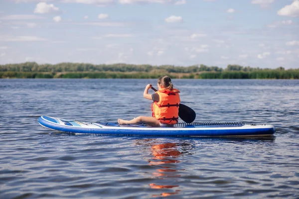 Sarışın, küçük bir kız gölde kürek çekiyor arka planda sazlıklar ve can yeleği giymiş ağaçlarla kürek çekiyor. Aktif tatiller. Çocukluktan beri spora olan aşkın kültürü