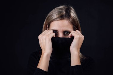 Siyah arka planda kameraya bakan endişeli, korkmuş kadın portresi. Fiziksel ve psikolojik tacize uğramış. İkna edici. Nispeten saldırganlık