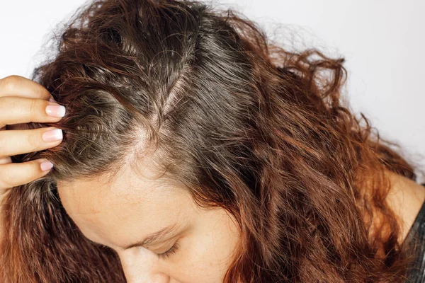 Nahaufnahme einer jungen Frau, die ergraute Haarwurzeln mit dem Kopf nach unten auf weißem Hintergrund zeigt. Nachwachsende Wurzeln, die einer Neufärbung bedürfen. Altershindernis. Kopierraum Stockbild