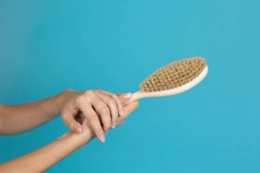 Mavi arka planda kuru deri masajı için ahşap fırçalı iki el. Selülitlerden kurtulma amaçlı anti-selülit prosedürleri. Kişisel bakım ve vücut bakımı