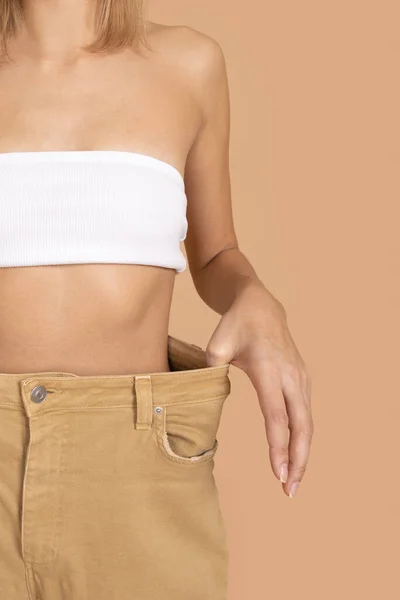 Close-up dari wanita Kaukasia ramping mengenakan celana kebesaran dan celana dalam bra putih menunjukkan pinggang ramping pada latar belakang kulit berwarna. Berat badan turun. Menjaga pola makan yang sehat, berolahraga — Stok Foto