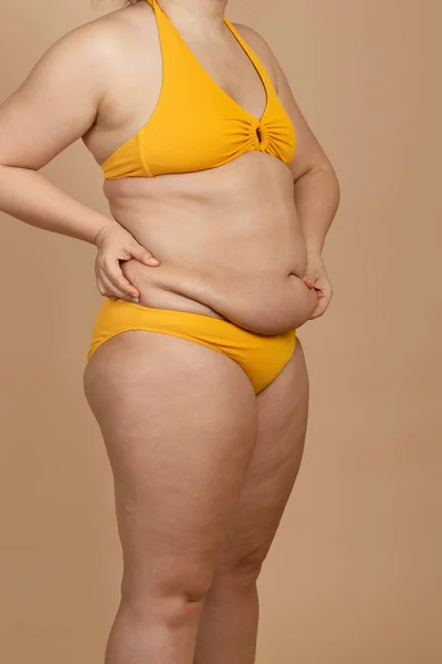 Zugeschnittenes Bild einer übergewichtigen, dicken Schwangeren mit Bauchläppchen, überschüssigem Fett im gelben Badeanzug. Schneller Gewichtsverlust Stockbild
