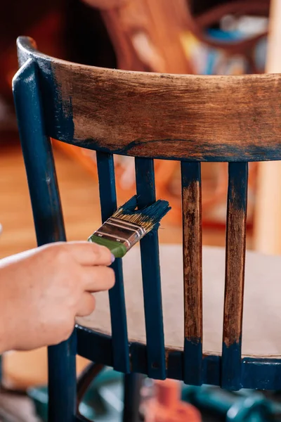 Nahaufnahme von Hand Malerei gealterten Stuhl in blauer Farbe mit Pinsel in der Werkstatt für Möbelsanierung. Wiederverwendung alter Dinge. Zukunft durch nachhaltiges Handeln denken lizenzfreie Stockfotos