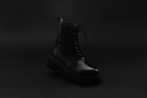 Egy elszigetelt fekete bőr őszi téli uniszex csizma áll fényes fekete háttér. Cipő sarokkal, kerek lábujjal és dombornyomott kemény talppal. Fénymásolási hely — Stock Fotó