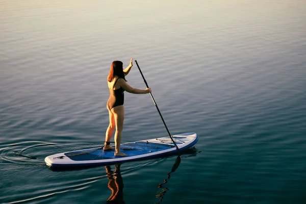 Вид зверху на розслаблену жінку середнього віку на дошці, що веслує з веслами на спокійній воді озера. Активний спосіб життя. Дозвілля для людей різного віку — стокове фото