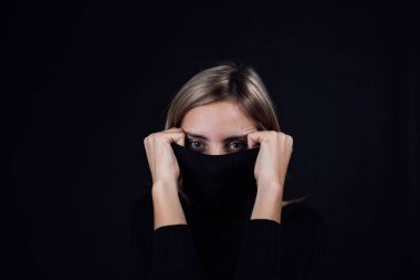 Yüzü siyah bluz yakalı, siyah arka plandaki kameraya bakan endişeli bir kadın. Fiziksel ve psikolojik tacize uğramış. İkna edici. Nispeten saldırganlık