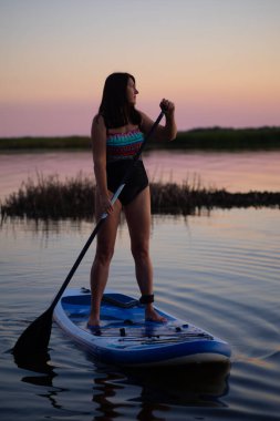 Orta yaşlı bir kadın mavi yemek masasına bakıyor. Akşamları arka planda pembe gökyüzü olan dalgalı bir göle kürek çekiyor. Yaşlılar için aktif yaşam tarzı