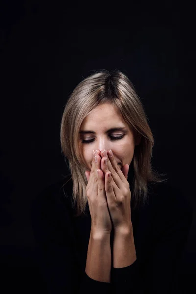 Frightened woman with hands hiding nose and mouth being silent dressed in black blouse on black background. Victim of physical and psychological abuse. Gaslighting. Relative aggression — Stock Photo, Image