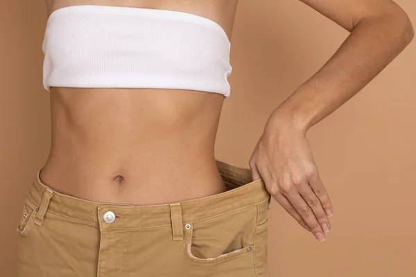 Fechar a cintura da mulher em jeans grandes oversize com a mão mostrando boa forma fina no fundo colorido do corpo. Perda de peso, mantendo a dieta e exercício — Fotografia de Stock