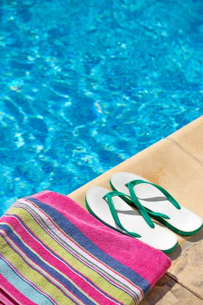 Coppia infradito e un asciugamano sul lato di una piscina — Foto Stock