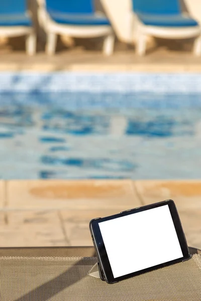 Blank digital tablet with empty space for text on a chair on the side of a swimming pool