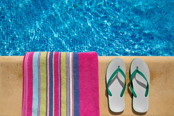 Шлепанцы и полотенце на стороне синего глубокого бассейна — стоковое фото