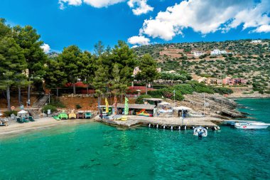 Kayalık sahile, kumlu plaja, deniz ve su spor istasyonuna, arka planda yeşillik. Bulutlarla güneşli bir gün. Seçici odak.