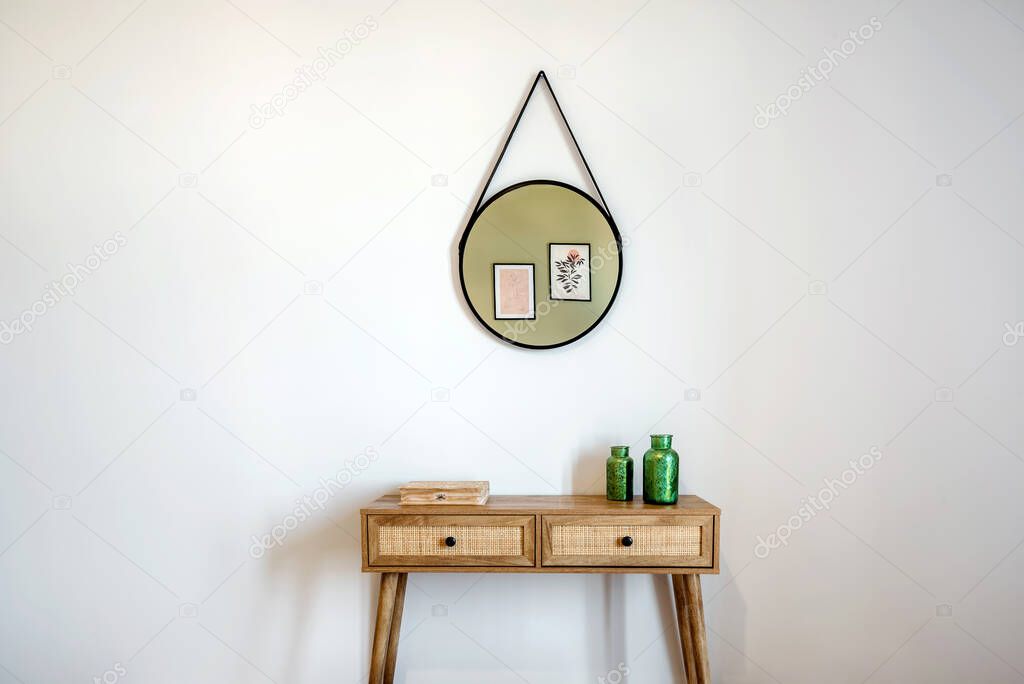Two-drawer wooden console with samll box and decorative green bottles on it. On the wall hanging decoration. 