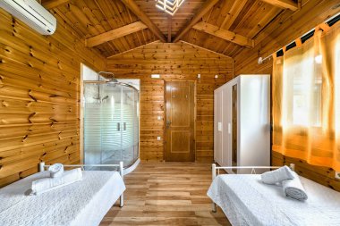 Banyo kabini olan bir yatak odası, ahşaptan yapılmış bir kır evi oteli. Tek kişilik yataklar, perdeli pencereler. 