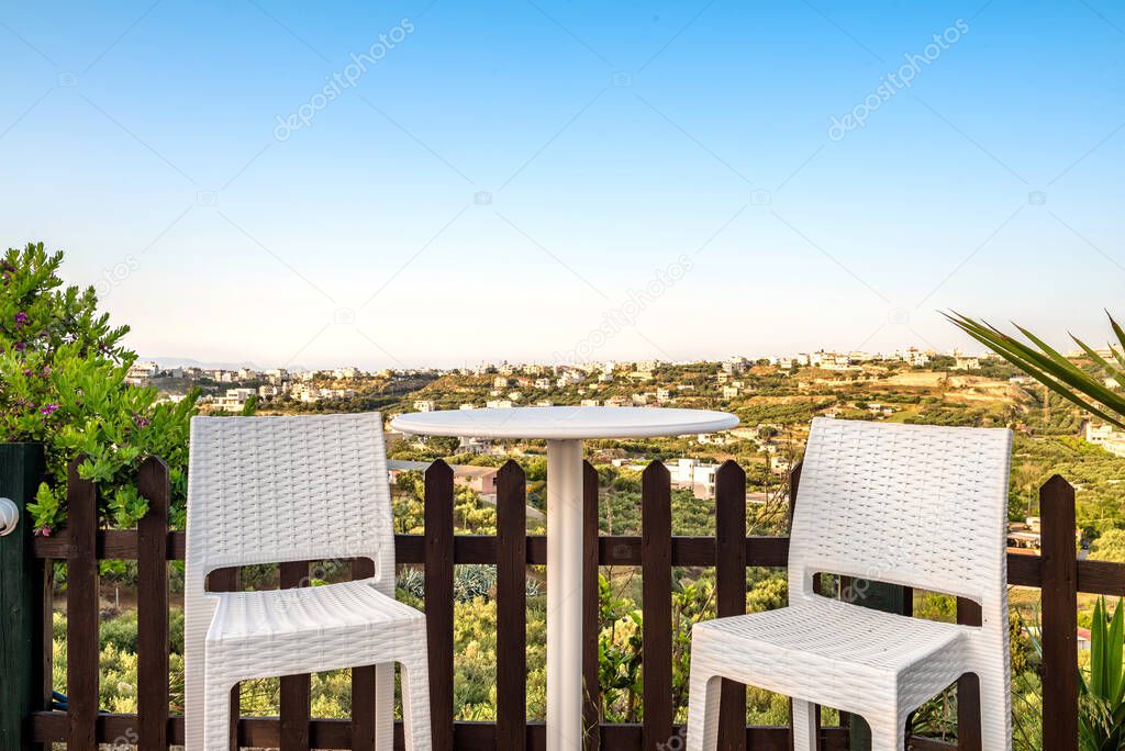 View to the terrace. There are two white chairs and table, garden furniture. Panoramic view to the area.