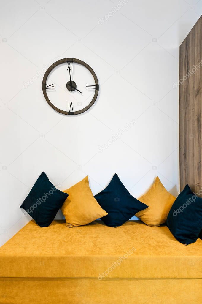 Living room interior design. Yellow sofa with yelow and black pillows on it. Modern clock on the wall. 